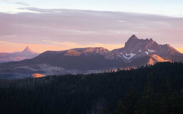A mountainous landscape appears purple and pink while the sun is either setting or rising. 